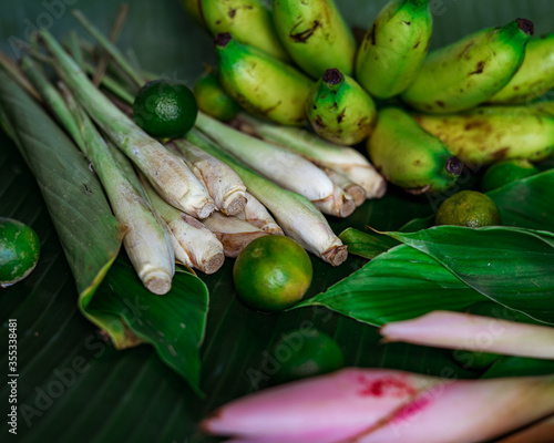 Asian food ingredients such as lemongrass, calamansi, tumeric leaves, torch lily and bananas on a banana leaf background.