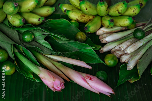 Asian food ingredients such as lemongrass, calamansi, tumeric leaves, torch lily and bananas on a banana leaf background.