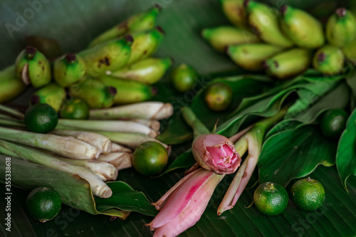 Asian food ingredients such as lemongrass, calamansi, tumeric leaves, torch lily and bananas on a banana leaf background.
