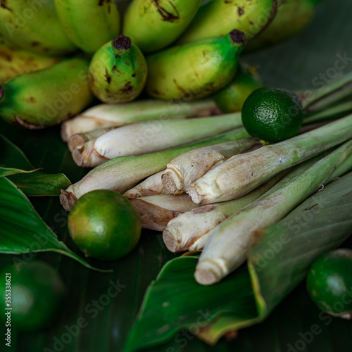 Asian food ingredients such as lemongrass, calamansi, tumeric leaves, torch lily and bananas on a banana leaf background.