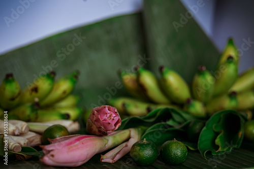 Asian food ingredients such as lemongrass, calamansi, tumeric leaves, torch lily and bananas on a banana leaf background.