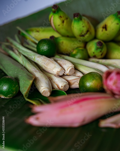 Asian food ingredients such as lemongrass, calamansi, tumeric leaves, torch lily and bananas on a banana leaf background.