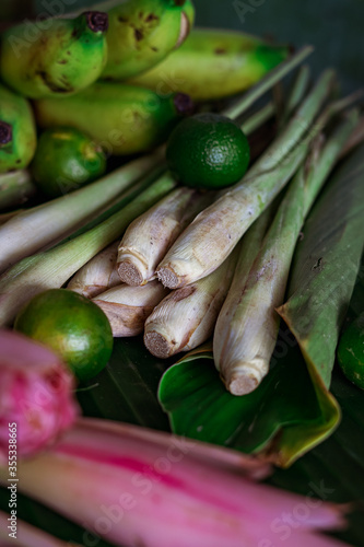 Asian food ingredients such as lemongrass, calamansi, tumeric leaves, torch lily and bananas on a banana leaf background.