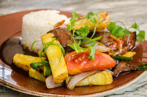 Lomo Saltado - A popular Chifa (Peruvian - Chinese) stir fry dish combining marinated beef sirloin, onions, tomatoes and french fries, served with white rice photo