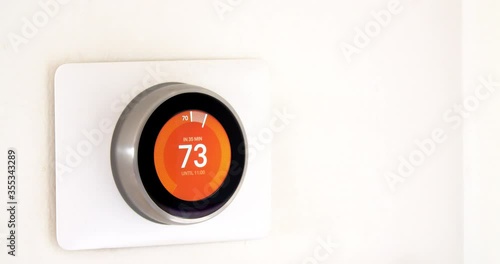 Calgary, Alberta, Canada. Jun 4, 2020.  A person hand saving energy on fahrenheit metrics using a Nest smart thermostat on a white wall. photo