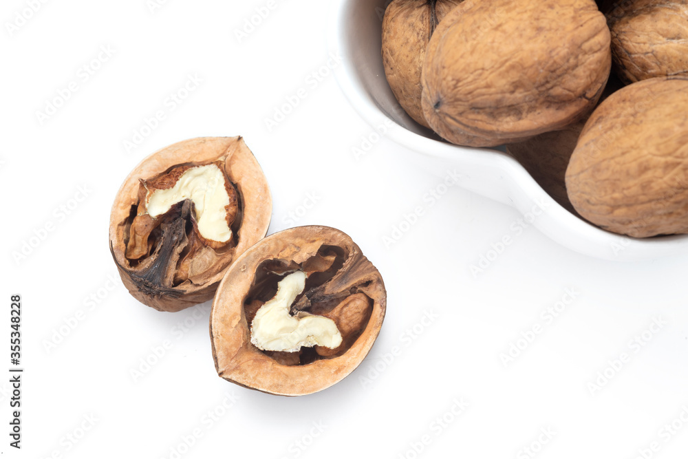 Walnuts in a white bowl and half of walnut next to the bowl. Clean surface. Top view | above, heart shaped nut. Isolated. Copy space for text editing, white background. Close up Walnuts in a white bowl and half of walnut next to the bowl. Clean surface. Top view | above, heart shaped nut. Isolated. Copy space for text editing, white background. Close up