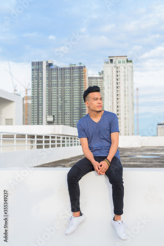 Full body shot of young handsome multi ethnic man sitting against view of the city