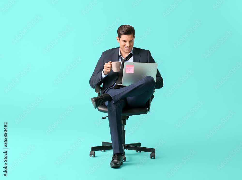 Young businessman with laptop and coffee relaxing on chair against color background Young businessman with laptop and coffee relaxing on chair against color background