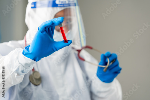 Scientist wear hazmat PPE protective clothing in lab coat,looking at test tubes with multi liquid in his arm. © visoot
