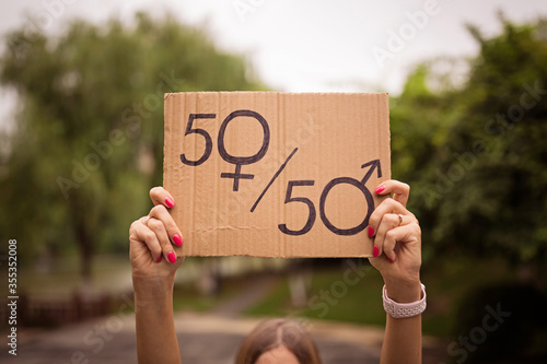 Cuadro en lienzo Gender equality concept as woman hands holding a paper sheet with male and female symbol over crowded city street background