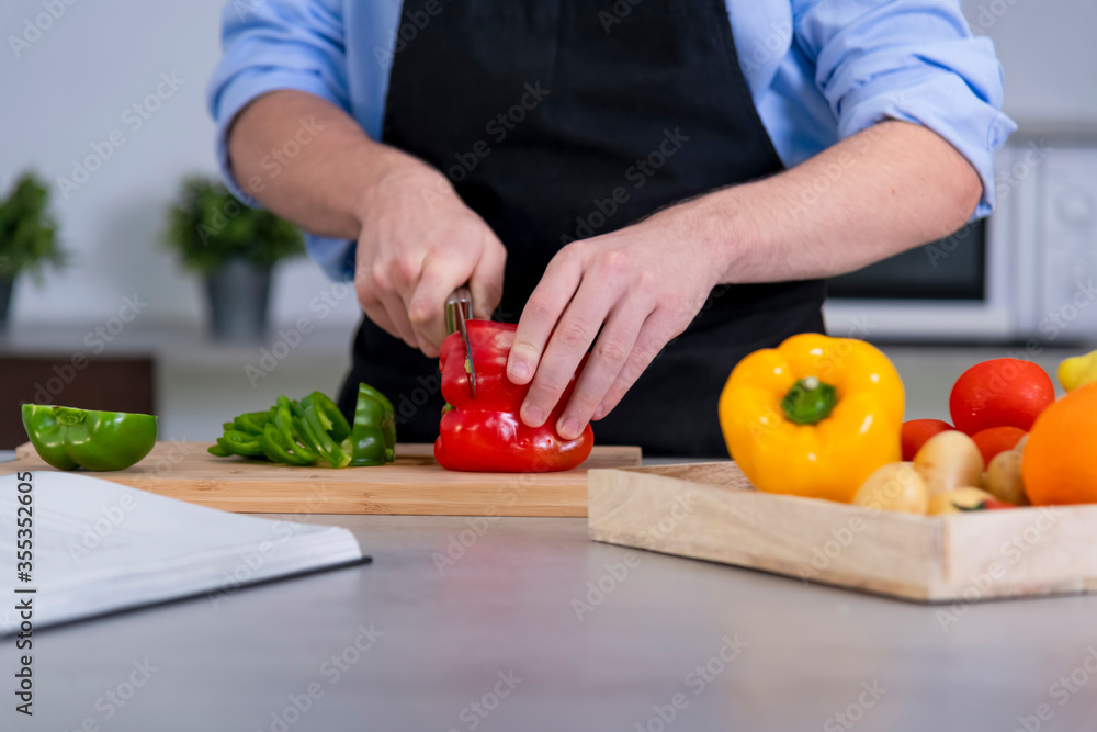 a young male cutting a red bell pepper on a cutting board surrounded by assorted vegetables a young male cutting a red bell pepper on a cutting board surrounded by assorted vegetables