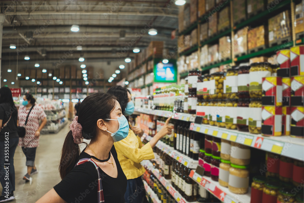Asian woman wearing face mask buying in supermarket. Young female panic shopping on shelf during Coronavirus covid-19 pandemic.