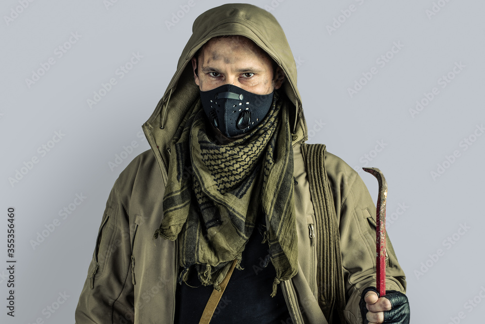 man with burglar crowbar wearing black protactive face mask and jacket with hood on gray background
