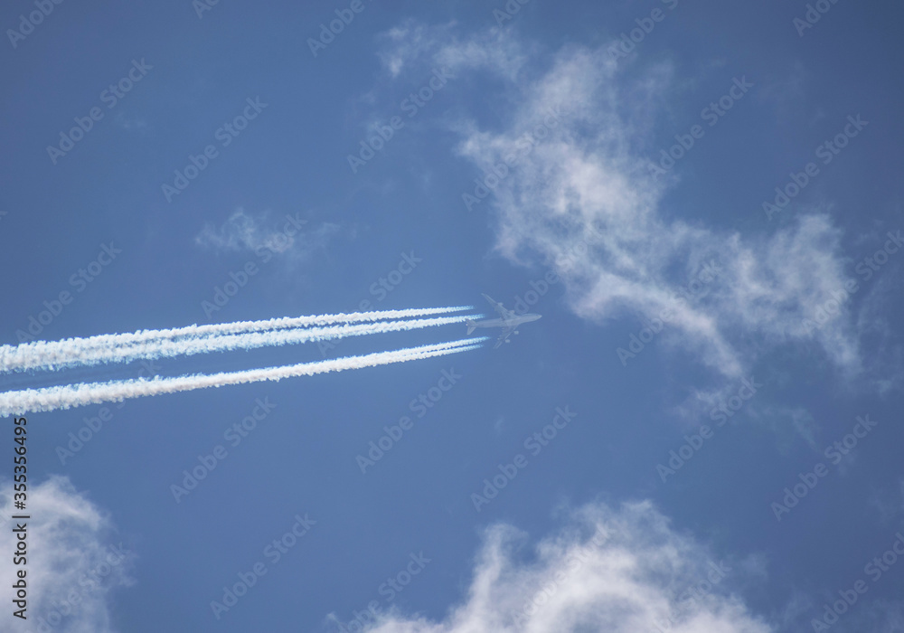 Traces of a four-engine commercial plane in the blue cloudy sky Traces of a four-engine commercial plane in the blue cloudy sky