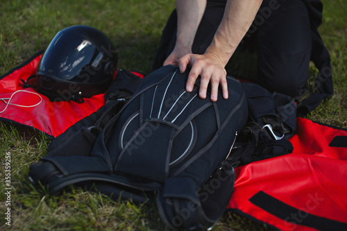 Packed parachute, skydiver hands and parachute equipment lying on green grass.