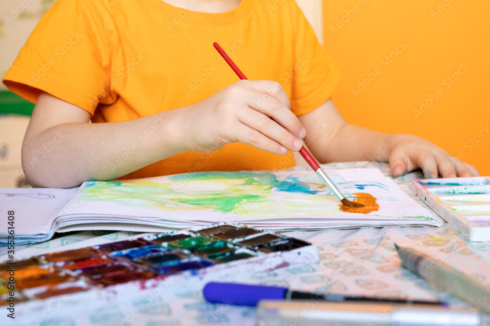 Naklejka premium art painting, childrens hands holding brush and drawing of orange paint.