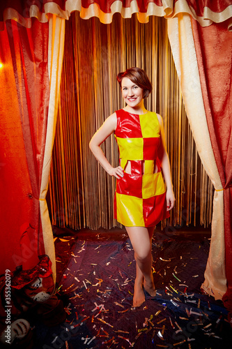 Young woman during a stylized theatrical circus photo shoot in a beautiful red location. Models posing on stage with curtain