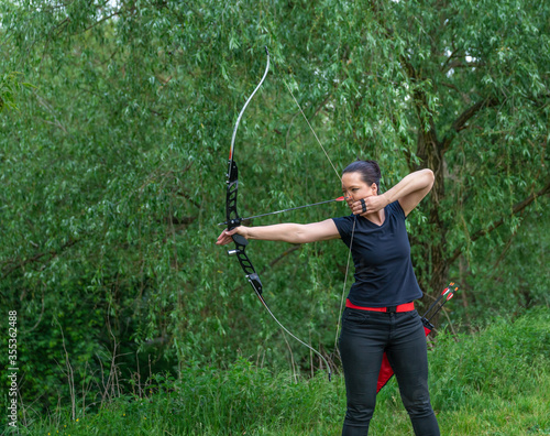 archery in nature. A young attractive woman is training in a bow shot with an arrow at a target in the woods