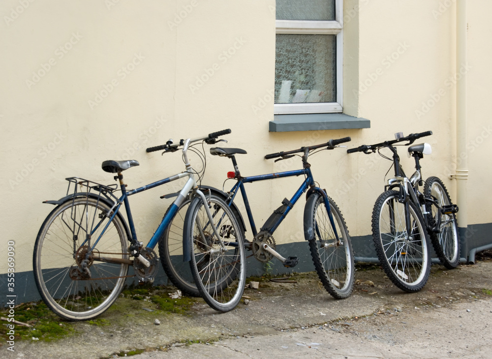 Three old rusty black bicycles leaning against a cream wall
