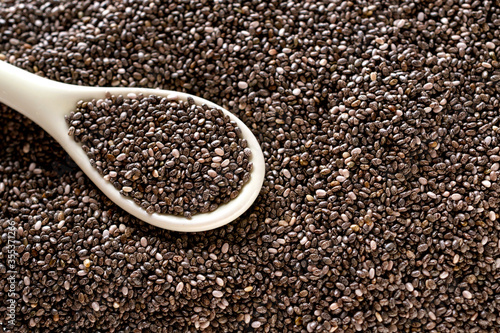Chia seeds in a white ceramic spoon on a pile of seeds top view.