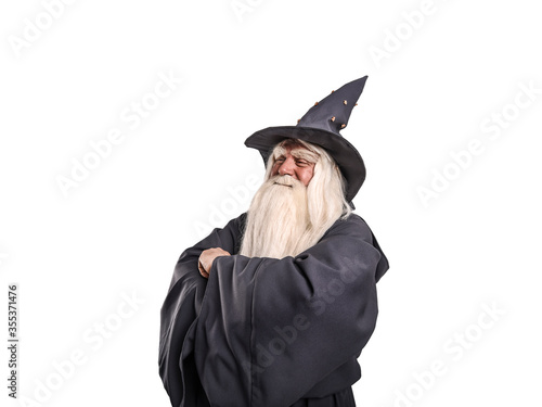A stern grey-haired bearded wizard in a gray cassock and a cap is practicing sorcery and doing magic against a light background.
