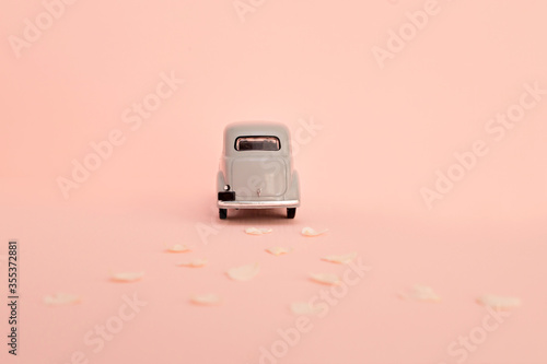 Gray retro toy car delivering flowers and gifts on a pink background. Copy space.