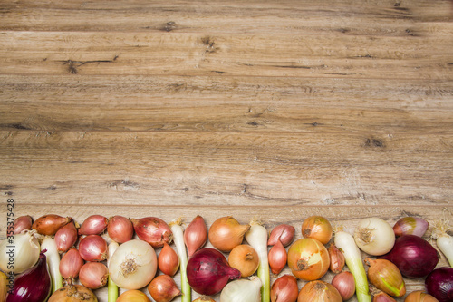  In the frame  onions  leeks  shallots  white  sweet red  yellow onions  green onions. Light wooden background. Close-up..