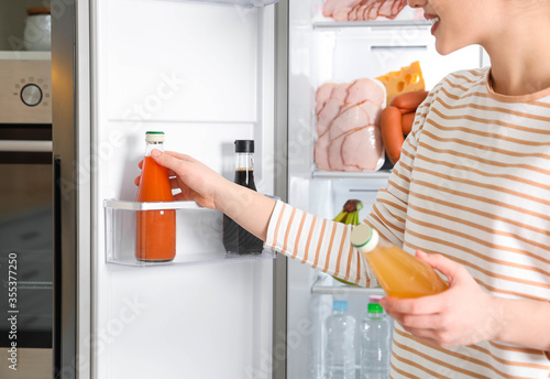 Young woman taking juice out of refrigerator indoors, closeup