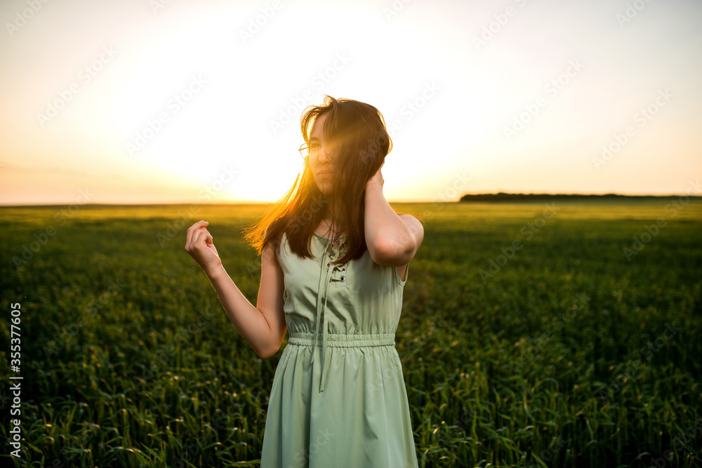 Obraz premium young, beautiful Asian girl in a field of green wheat on the background of the sunset