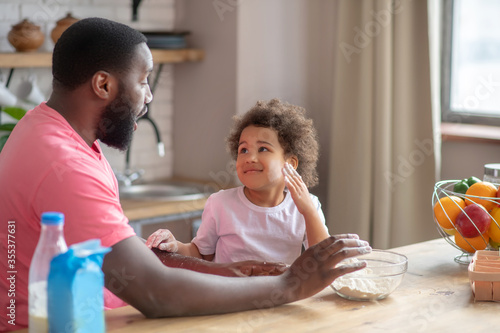 Dark-skinned father having fun with his daughter in the kitchen