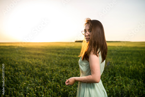 young, beautiful Asian girl in a field of green wheat on the background of the sunset
