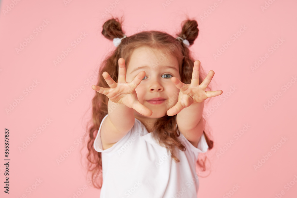Portrait of surprised cute little toddler girl child over pink background. Looking at camera. Points hands to the left side. Advertising childrens products Portrait of surprised cute little toddler girl child over pink background. Looking at camera. Points hands to the left side. Advertising childrens products