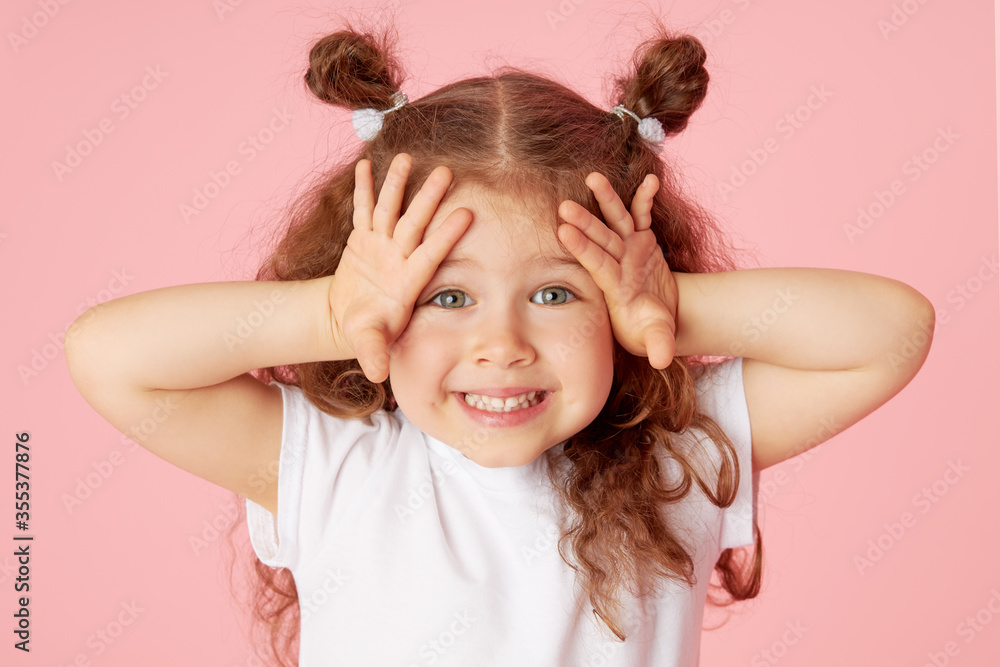 Portrait of surprised cute little toddler girl child over pink background. Looking at camera. Points hands to the left side. Advertising childrens products Portrait of surprised cute little toddler girl child over pink background. Looking at camera. Points hands to the left side. Advertising childrens products