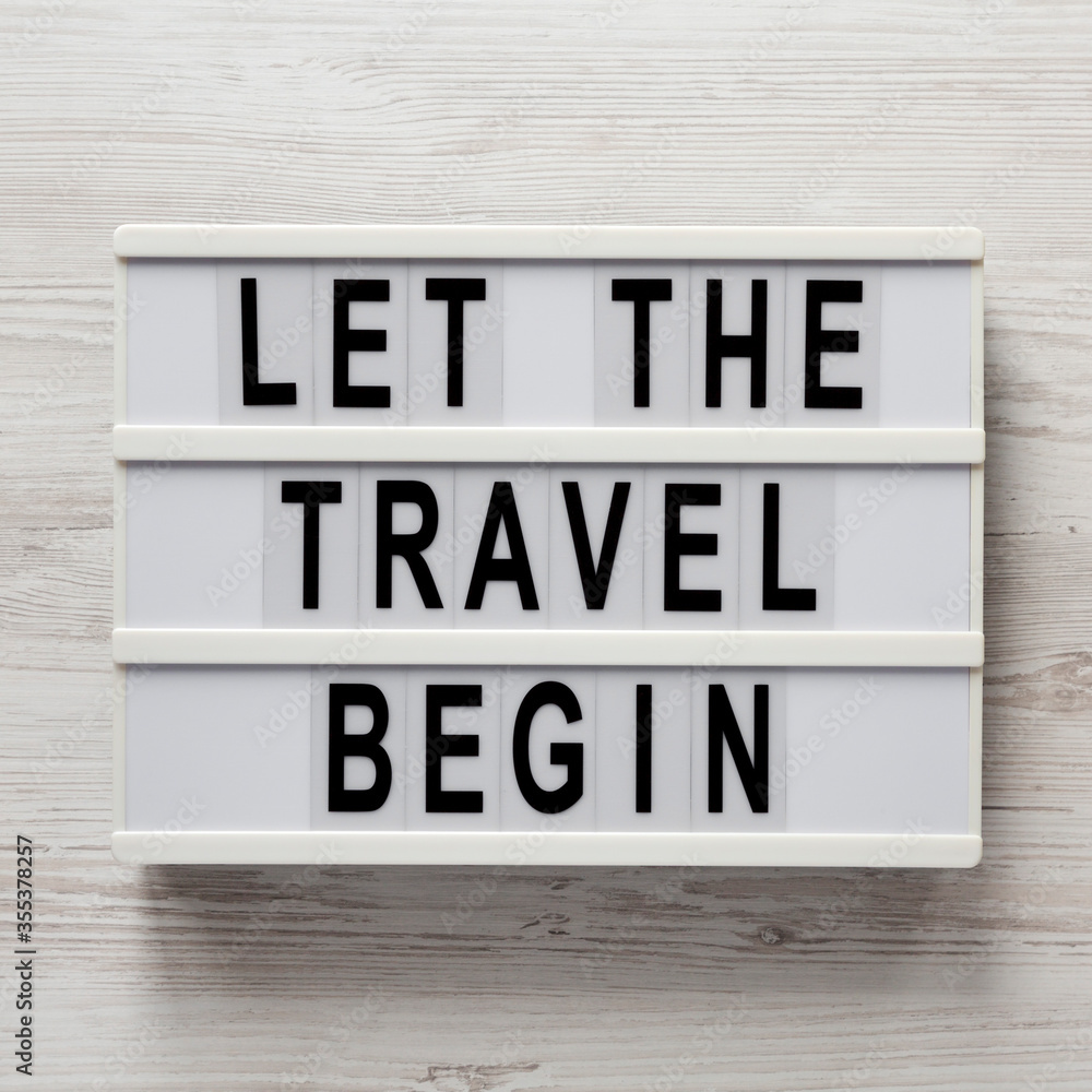 'Let the travel begin' on a lightbox on a white wooden background, overhead view. Flat lay, from above, top view. 'Let the travel begin' on a lightbox on a white wooden background, overhead view. Flat lay, from above, top view.