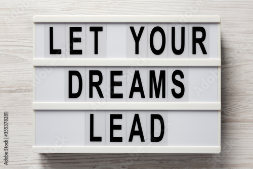 'Let your dreams lead' on a lightbox on a white wooden background, top view. Flat lay, from above, overhead.