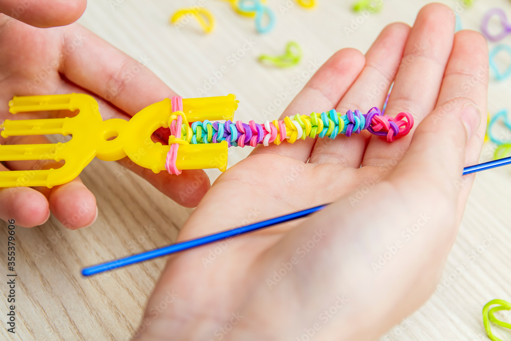 Fototapeta premium Rubber Band Weaving. Knitting rubber bands with loom knit. Hands of girl weaving wristband of rubber bands.
