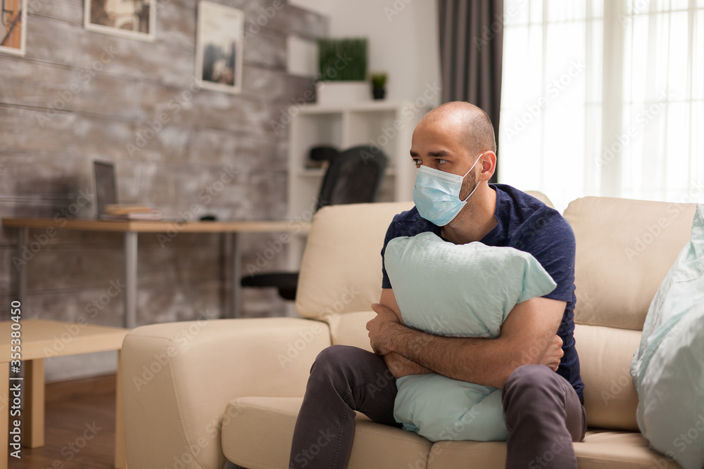 Anxious man holding tight a pillow during self isolation wearing disposable mask. Anxious man holding tight a pillow during self isolation wearing disposable mask.