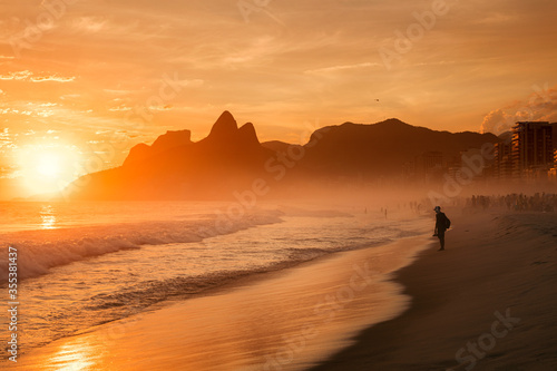 Silhouette of the lonely man on Ipanema beach with Dos Irmaos on the background during the sunset in Rio de Janeiro, Brazil.