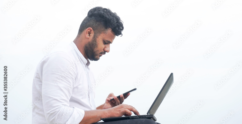 young man using laptop and smart phone together young man using laptop and smart phone together