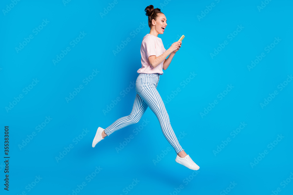 Full length body size view of her she nice-looking attractive pretty lovely glad cheerful cheery girl jumping using digital device 5g app isolated on bright vivid shine vibrant blue color background