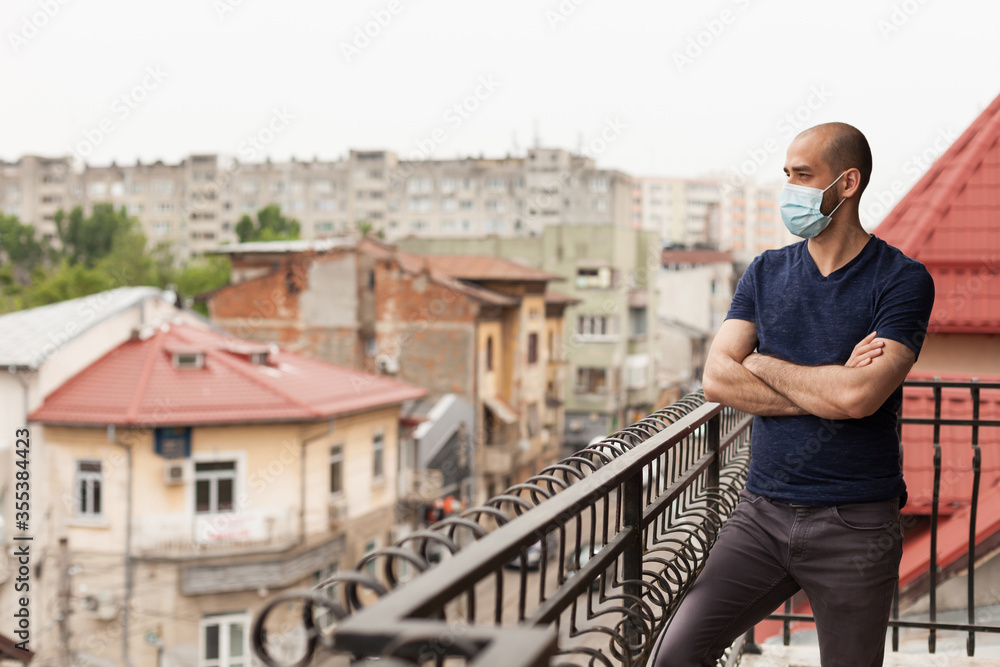 Guy with prevention mask on apartment balcony during global pandemic. Guy with prevention mask on apartment balcony during global pandemic.
