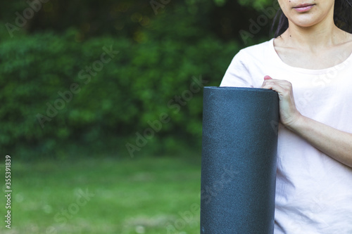 Young woman holding yoga mat in the park