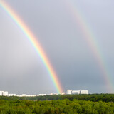 double rainbow over green forest and city on spring day