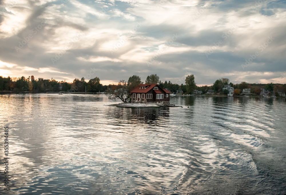Fototapeta premium sunset on the river, small island floating house, waves, water reflection in 1000 islands