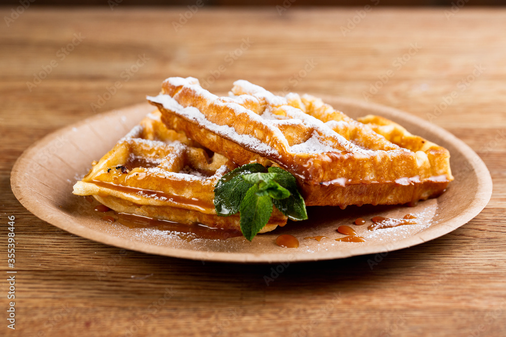 .Viennese waffles on a disposable plate with strawberry jam, icing sugar and mint. cook decorates dessert with icing sugar