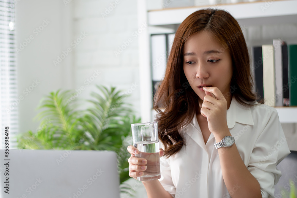 Asian business women drinking water and taking medicine. She feels sick. Asian business women drinking water and taking medicine. She feels sick.