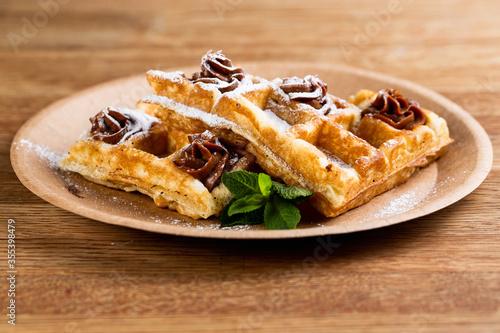 .Viennese waffles on a disposable plate with peanut butter, icing sugar and mint.