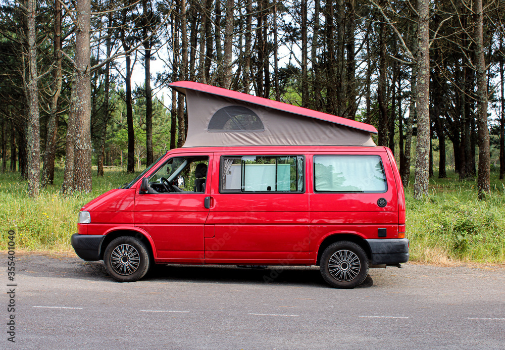 Red Van with roof up. Campervan parked next to forest.