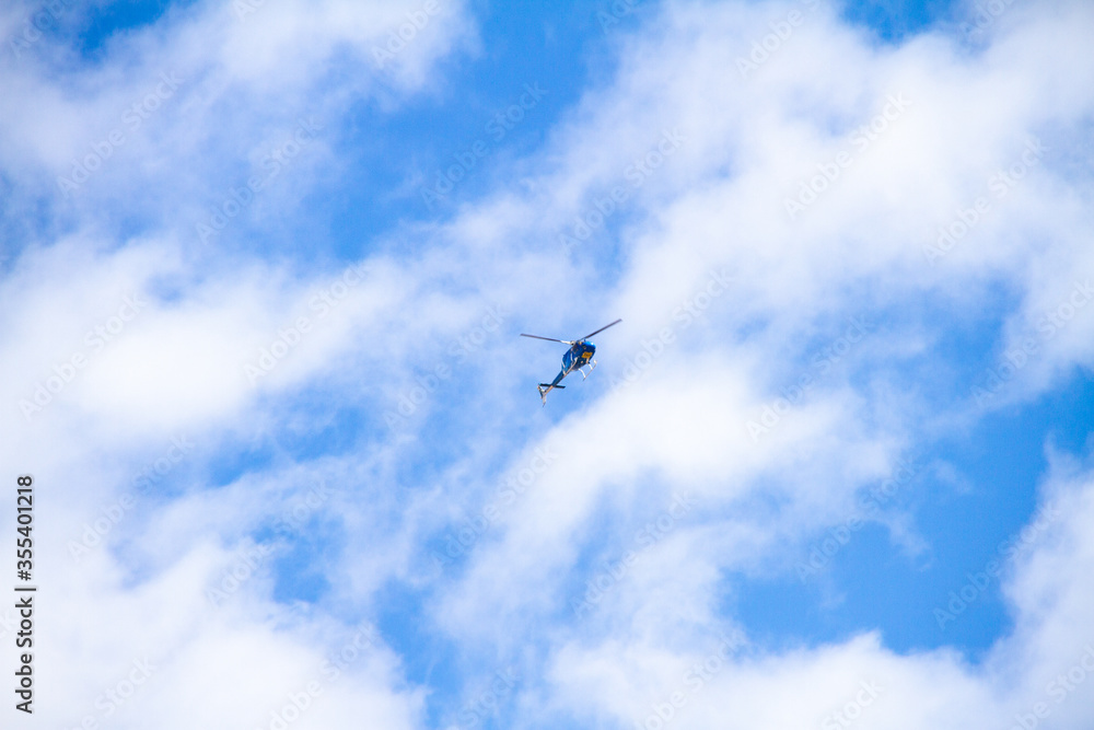 Helicopter flying on sunny day with blue sky and clouds