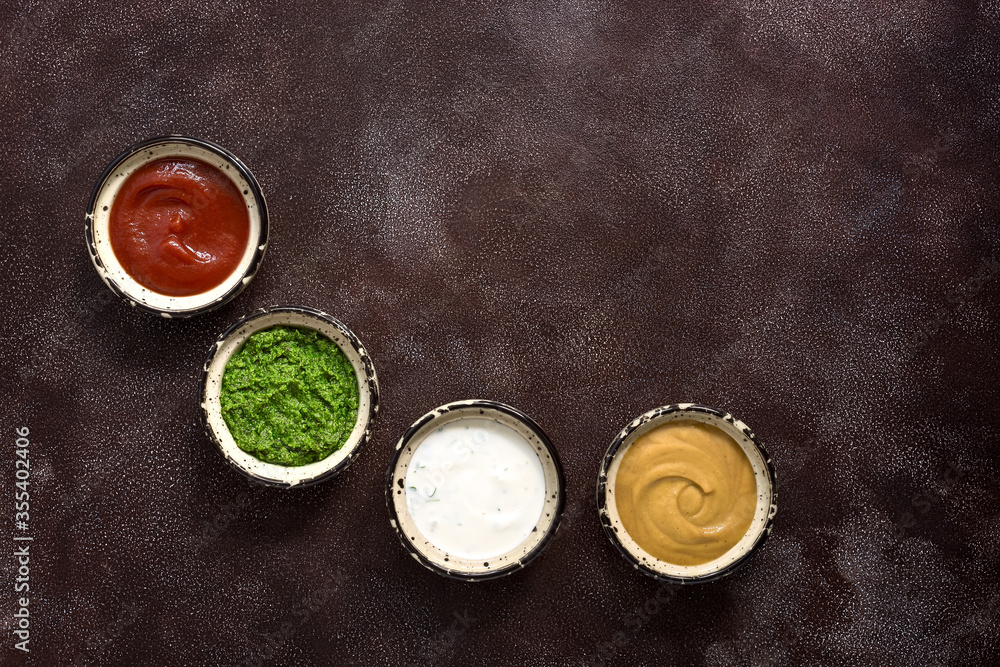 Assorted different sauce in the bowl: tomato, pesto, creamy with greens and mustard on a dark rustic background. Top view, copy space. Assorted different sauce in the bowl: tomato, pesto, creamy with greens and mustard on a dark rustic background. Top view, copy space.